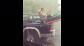 Man pretends to kayak on the back of his truck in the pouring rain