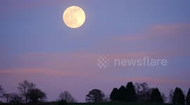 Spectacular full worm moon rising over the Wirksworth valley in the Derbyshire Dales with pink rays of the sunset shining on the clouds.