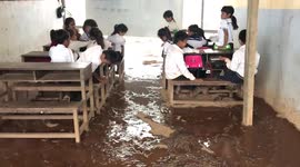 Students sit in muddy flooded classroom during rainstorm in Cambodia