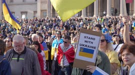 A crowd of people standing with a person holding a 'Stand with Ukraine' placard at the London Stands with Ukraine: March and Vigil