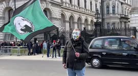 Protester wearing Guy Fawkes mask waves Anonymous flag outside Downing Street
