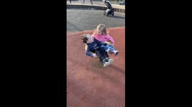 2 toddler friends play in an outdoor play park - laughing as they are spinning faster