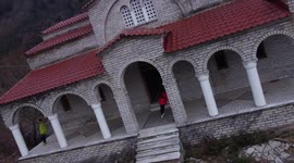 Tourists attempt to stand upright on church slowly sinking down hill in Greece