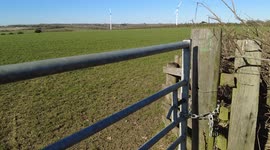 Looking over a gate to view the wind turbines in a field in slow motion