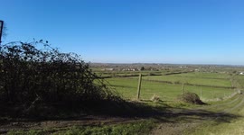 A time-lapse video of a stunning countryside view. Camera pans a woman can be seen walking her dog. Sunny day shot in rural England. Spring 2022