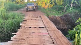Skillful driver moves heavy pickup truck across narrow bridge made from wooden planks