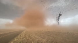 Storm chaser drives alongside large tornado with swirling clouds of dust through Texas