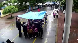 Teachers hold aloft waterproof mat as they escort students to gate during downpour in China