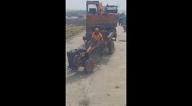The driver using a small tractor to transport a large excavator, surprising many people