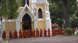 Thai Buddhist monks and people walk around a temple three times carrying candles and flowers to celebrate Vesak Buddha Day.