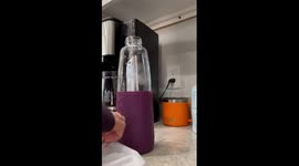 ASMR video of ice cubes and cold water being poured into a drinking glass by a woman’s hands in the kitchen.
