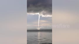 Spectacular waterspout tornado pierced by golden sunlight at dawn