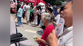 Elderly woman waits for grandson outside exam centre with sweet dessert