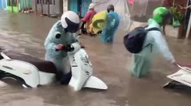 Motorcycle riders push their bikes through flooded road in Cambodia