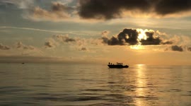 Long shot of fishing boat captain tossing a cast net at sunrise.