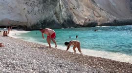 Bathers crawling ashore on all fours to step out of the sea at a beach in Greece