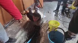 Workers use pneumatic drill on concrete floor to save blind dog stuck in water pipe