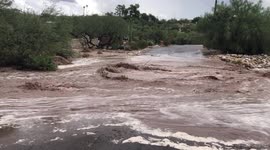 Flash flood in Tucson Arizona destroys road. debris can be seen floating down stream. families can't get to their homes