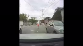 Man rides electric scooter through streets with child sitting on his shoulders
