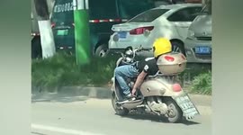 Easy rider! Motorist lays on scooter without holding handlebars in China
