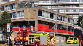 Firefighter smashes glass out to run hose to a fire in a building in London's Elephant and Castle
