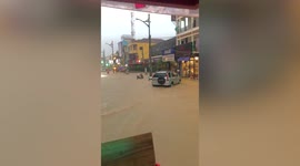 Tourists party in tuk-tuk driving through flooded road in Cambodia