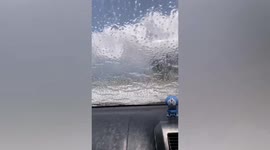 Huge waves crash onto car driving along beachside road