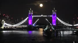 Full harvest moon rises over London Tower Bridge, lit up in purple to remember Queen, as it opens to allow boat to pass