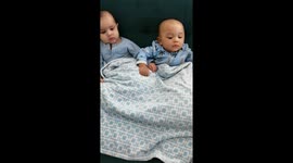 Two baby cousins one month apart being entertained by the grandmother holding a rattle