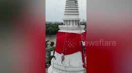 Devotees climb 100ft Buddhist chedi to wrap sacred red cloth around its spire