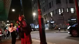 A homeless women sings with backup music to people outside Sexy Fish restaurant in Mayfair