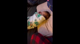 Newborn baby boy pauses and smiles warmly after being swaddled by mom.