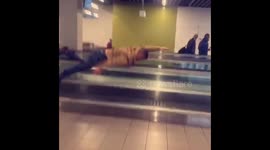 Lad entertains mates by 'swimming' along travelator hand rail at Schiphol airport