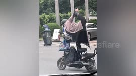 Woman holds yoga pose whilst riding scooter along road in China