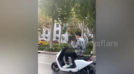 Man rides scooter along busy road while playing on his phone in China