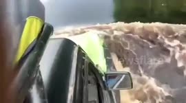 Cars drive through river-like flood along road in Indonesia