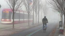 Bicyclist and electric scooter disappearing into thick fog using the Toronto downtown waterfront trail.