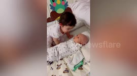 Cute toddler kisses and waves at newborn baby brother after seeing him for first time