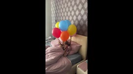 A girl with floating balloons tied to her hair is waiting for her brother's birthday!