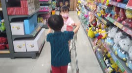 Adorable moment of a toddler pulling sitting in trolley sister having toys shopping