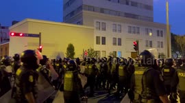 Dozens of riot police move in formation towards protestors whilst firing tear gas into the air