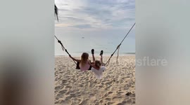 Holiday fail! Kids topple backwards from beach swing onto sand