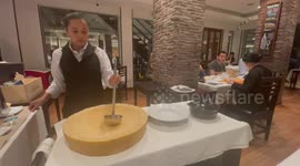 Waitress serves delicious pasta from flaming parmesan cheese wheel