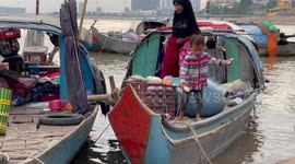 Children play on wooden fishing boats while parents sell the morning's catch
