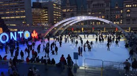 Crowd of people ice skating in circles at Toronto City Hall Nathan Phillips Square ice rink during winter holiday.