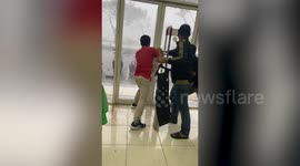 Frantic staff grapple with shop's glass door to keep it closed during freak storm in Indonesia