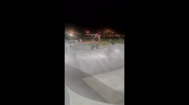 A BMX rider at the skatepark drops in a bowl and attempts a flair trick before bailing at the last second