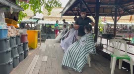 Locals have their hair cut by outdoor barbers next to river in Thailand