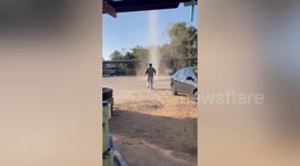 Playful driver jumps through dust devil tornado swirling through car park