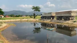 Bungling driver spills trailer full of sand into pond while making sharp turn